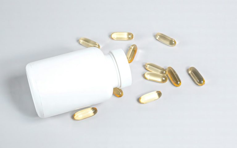 Flacon de compléments renversé, gélules de biotine éparpillées sur fond clair