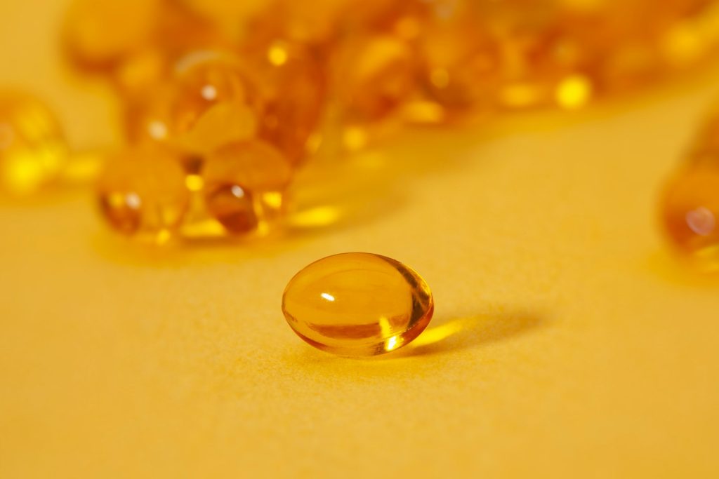 Gélules de complément alimentaire translucides, jaune doré, disposées sur un fond bleu clair