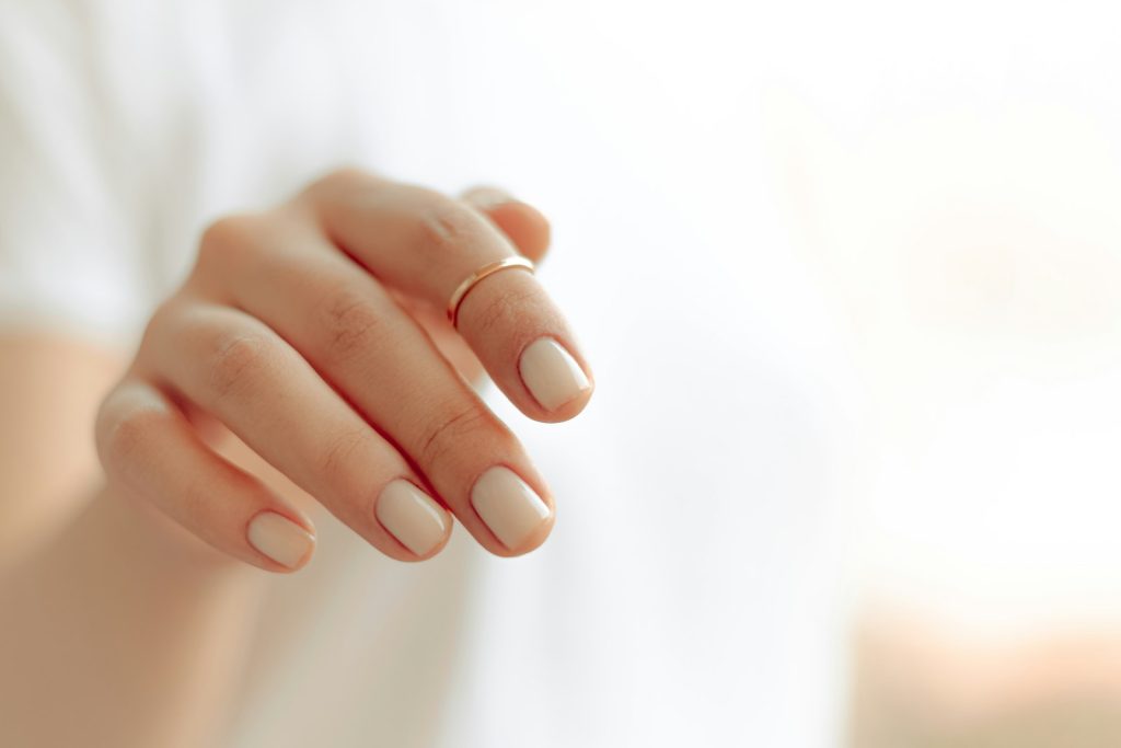Gros plan sur une main de femme aux ongles courts et manucurés, posée sur fond clair
