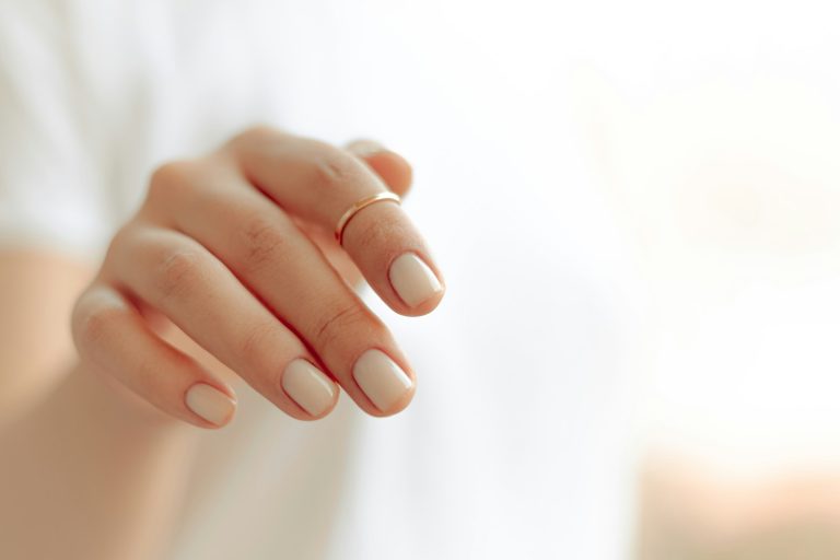 Gros plan sur une main de femme aux ongles courts et manucurés, posée sur fond clair