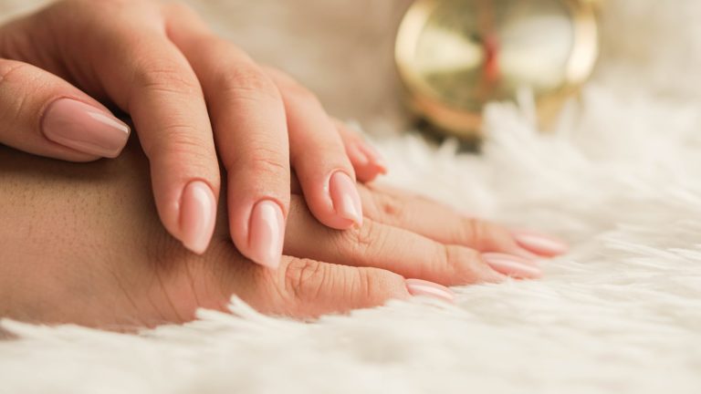 Ongles striés d'une main de femme vus de près, posée sur un tissu clair